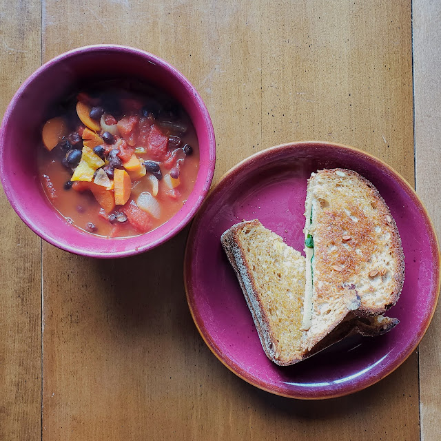 A bowl of hearty vegetable soup and a vegan grilled cheese sandwich with tzatziki, spinach, and Tofurkey slices