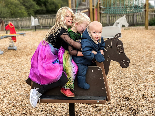 3 children on a rocking horse in a playground taken by a mum of 3 blogger for Instagram