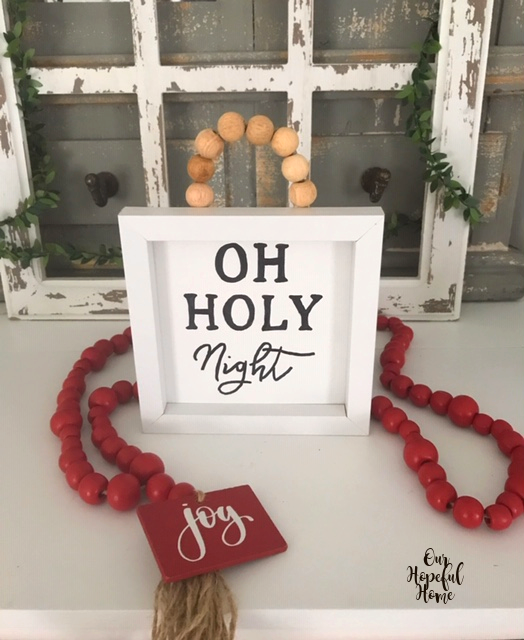 Oh Holy Night sign with red bead garland wrapped around it.