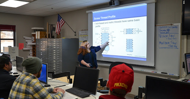 woman instructs at board with students in foreground