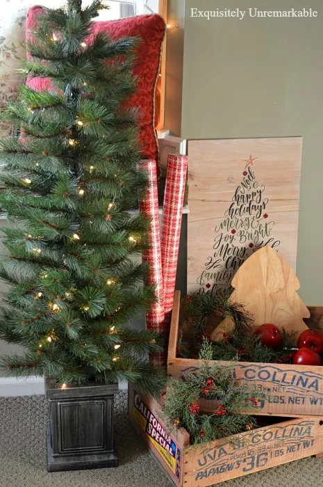 Small prelit Christmas Tree in an urn next to wood crates with wrapping paper and wreaths