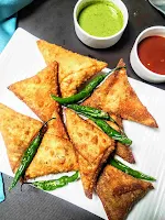 Serving samosa with fried green chili, sweet chutney and green chutney in background