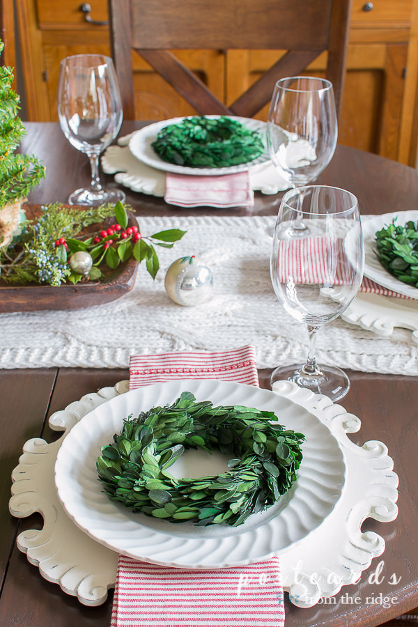 table set with white dishes, red and white striped napkins, and little preserved boxwood wreaths