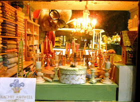 Looking through the front window of a miniature shabby chic shop with the owner peeking in from the back,