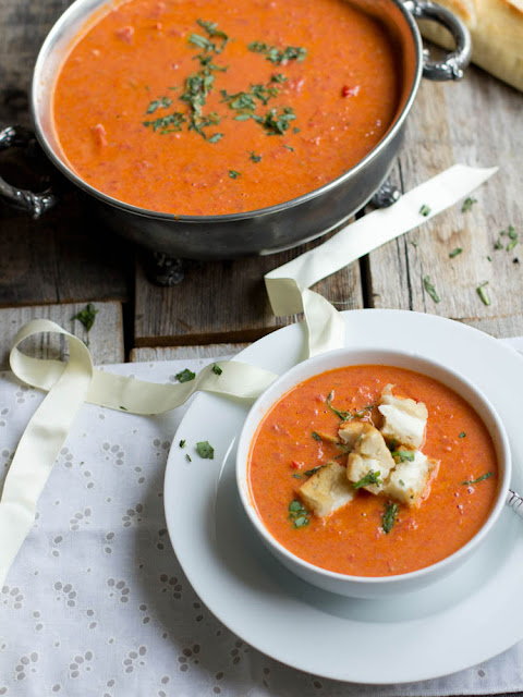a bowl of roasted tomato basil soup topped with grilled cheese croutons. A pot of soup sits in the back
