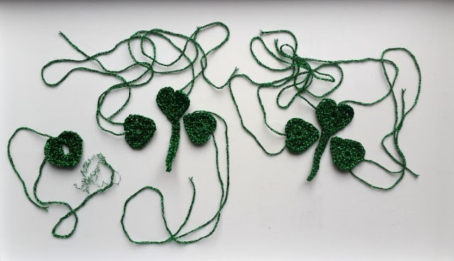 This photo shows the components of the shamrock including the first attempt on the left.  Each finished shamrock is made of three components: two heart-shaped leaves plus one heart-shape with a stem attached. Stitch the three elements together at the stem and heart points.