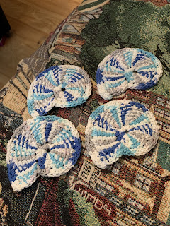 4 Tunisian crochet seashell shaped cloths. The yarn is white with splashes of gray, aqua, and blue. Each one is subtly different due to the color placements.