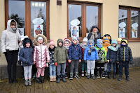 Grupa przedszkolaków z balonikami stoi przed okani biblioteki w Zelowie.