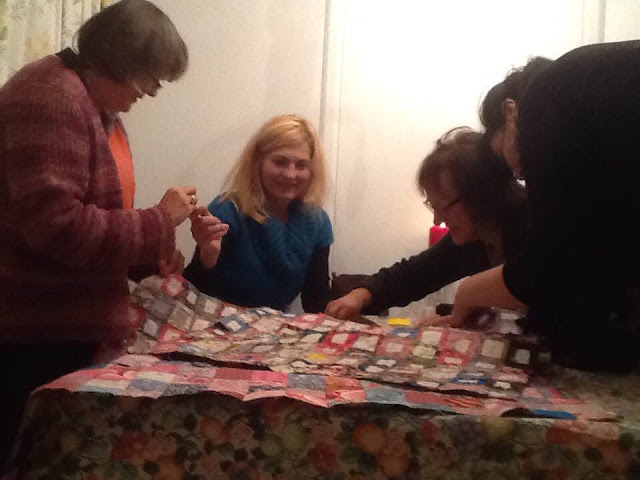 4 women sewing a quilt at a table