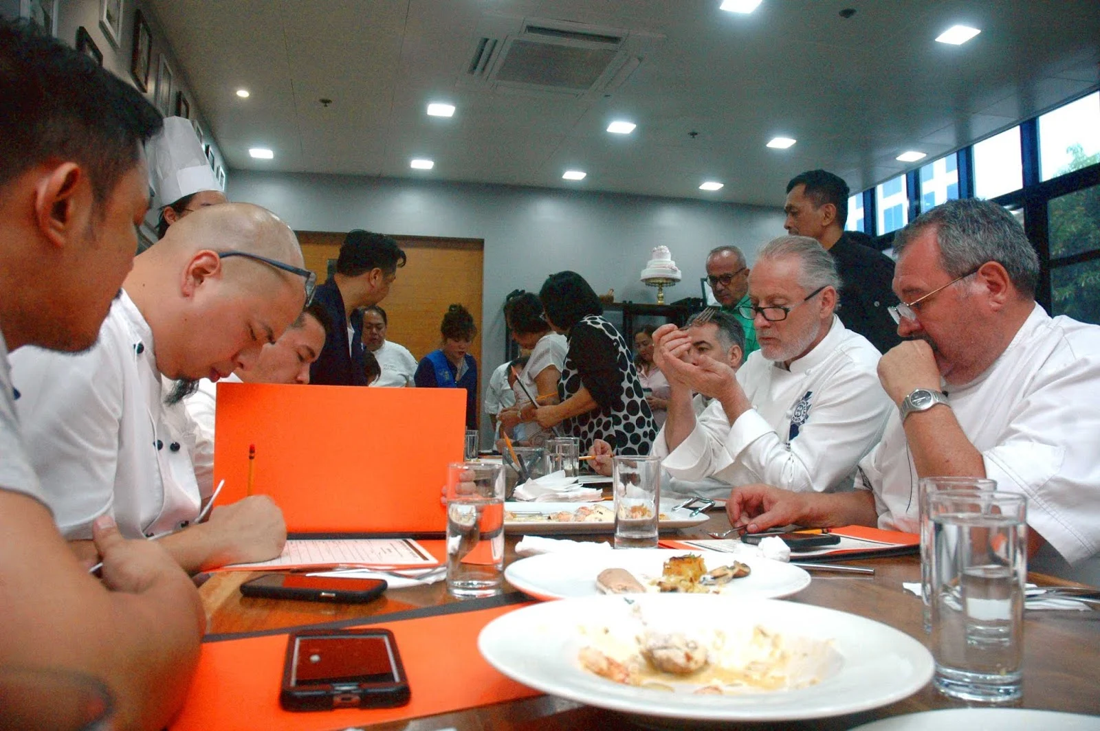 A panel of judges sitting at a table, tasting food and taking notes.