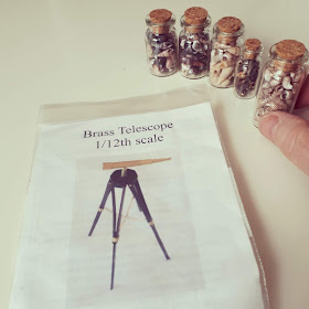 1/12 scale brass telescope kit next to five small jars of tiny shells. A hand is picking up one of the jars.
