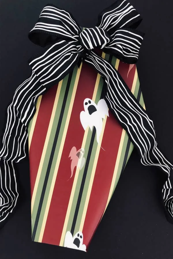 Halloween gift in shape of coffin wrapped in striped ghost paper with black and white striped ribbon and bow