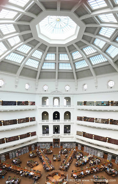 Library visitors at wooden tables in a six-storey high octagonal reading room under a white glas dome.