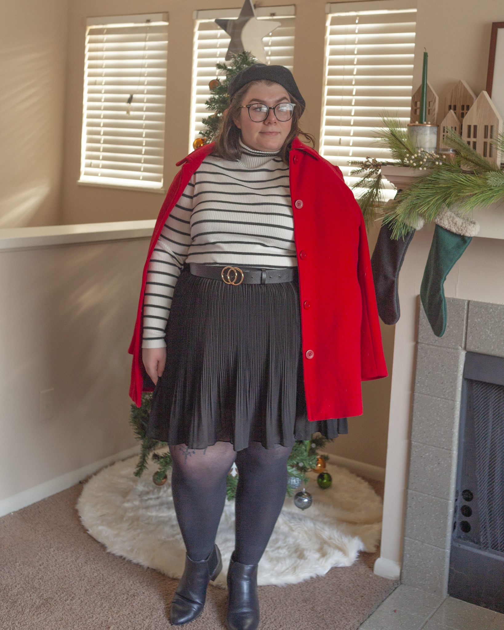 An outfit consisting of a black beret, a red peacoat draped over the shoulders, a black on white striped turtleneck tucked into a black pleated mini skirt with sheer black rights and black chelsea boots.