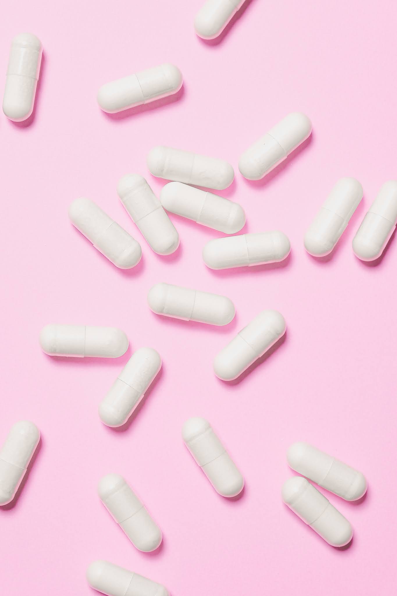 Vitamins scattered on pink background