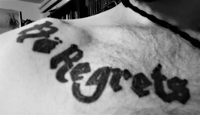 Tattoo unter dem Schlüsselbein mit dem Schriftzug "Nö Regrets" in der Schrift von Motörhead