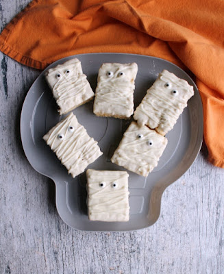 Super fun and easy to make mummy rice crispy treats are cute for Halloween party treats. Plus the kids can help make them! skull shaped platter filled with rice krispie treat mummies