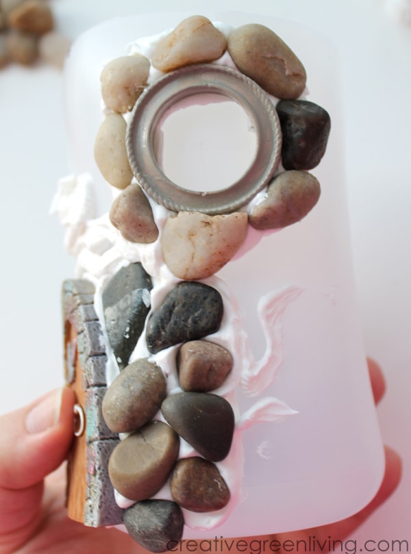 stone fairy house in progress - round window frame with small stones around the outside and decoden clay peeking through inside