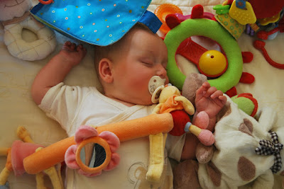 Śpiące w łóżeczku niemowle otoczone zabawkami