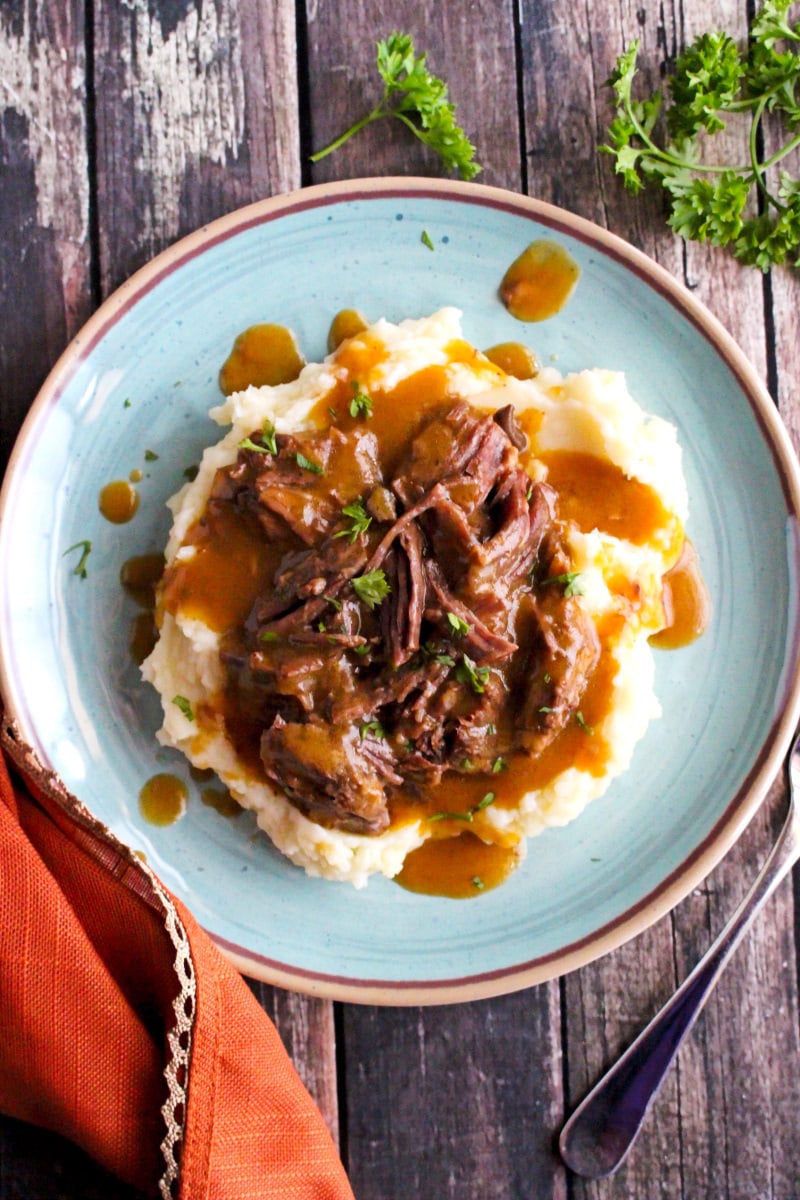 Instant Pot Shredded Beef and Gravy on a plue plate on a rustic wood background.