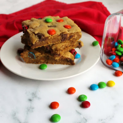 three pieces of chewy salted caramel m&m blondies stacked high on plate with candies scattered around