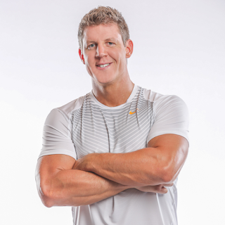 author Joel Marion, a muscular man with short blonde hair smiles while wearing a white athletic shirt against a white background