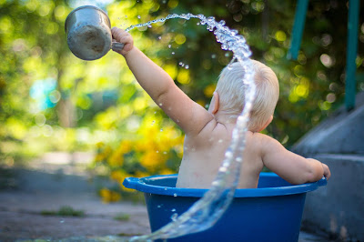Baby In Tub in Garden using a cup to poor splash out water: This article is about how to help your child start swim lessons
