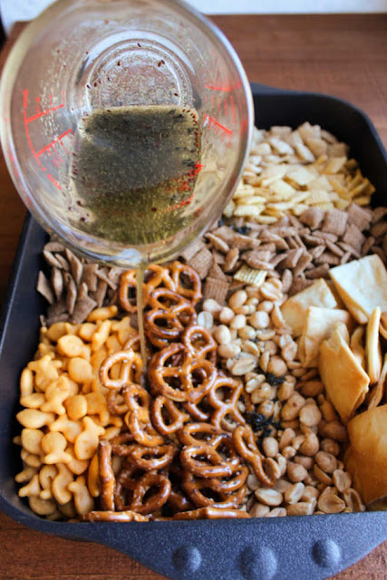 pouring garlic and dill oil mixture over cereal bits in pan