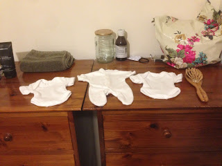 A tiny premature-size babygrow and two vests alongside a hairbrush for size comparison, on a couple of chests of drawers.