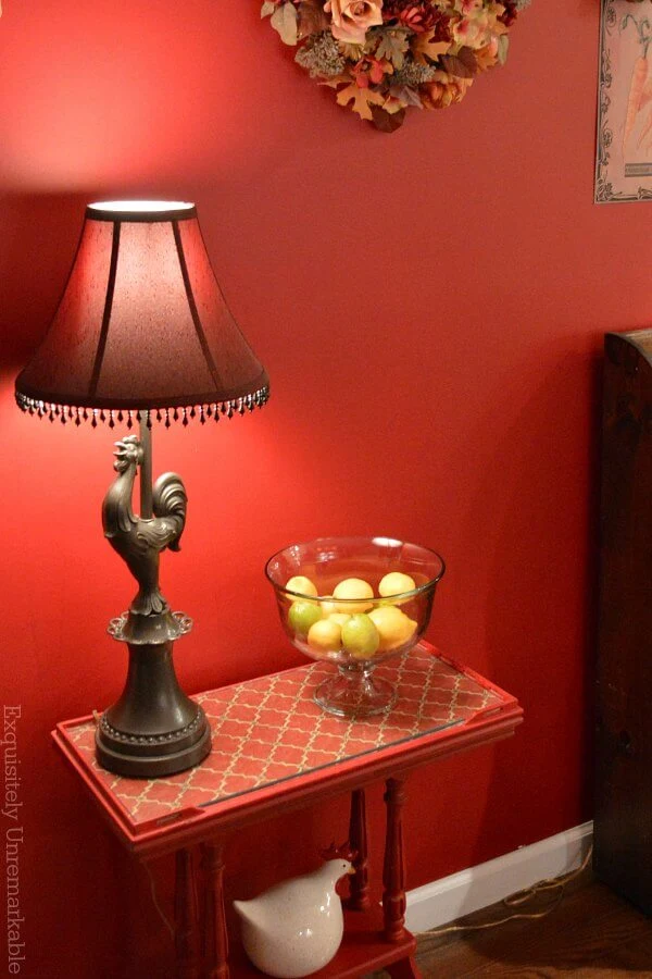 Small red painted table in the hallway with rooster lamp and lemon bowl on it