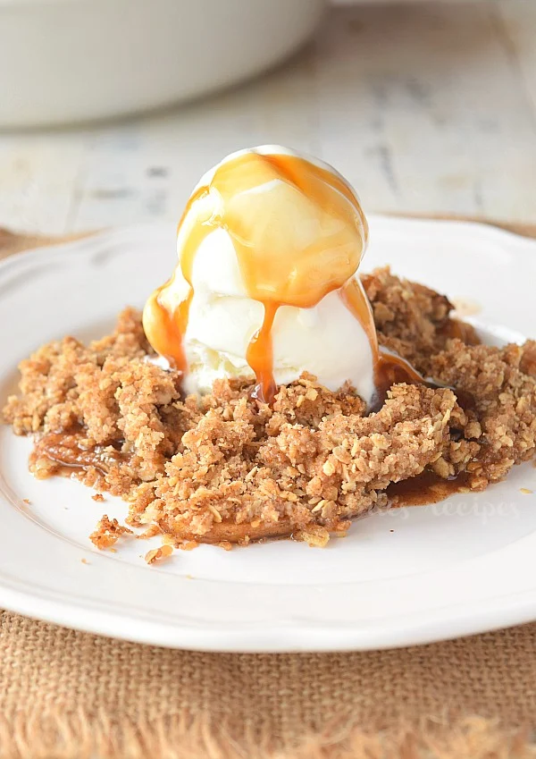 a white plate with apple crisp topped with vanilla ice cream and caramel