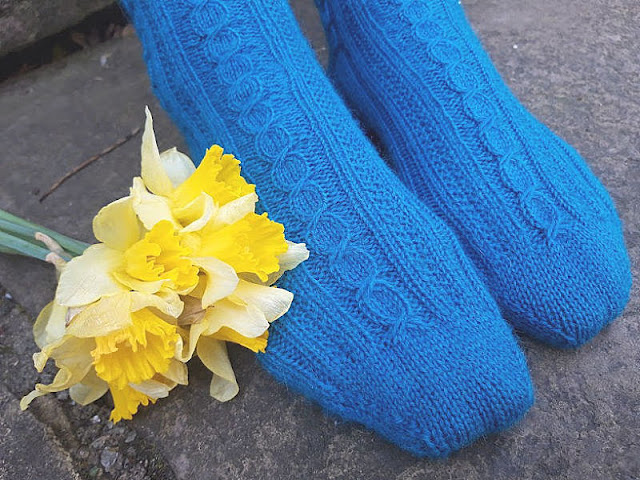 Photo shows a pair of blue patterned socks next to a bunch of yellow daffodils