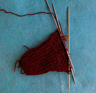 A mitten in progress on double-pointed needles.   Mitten is knit in red-brown fingering-weight yarn.