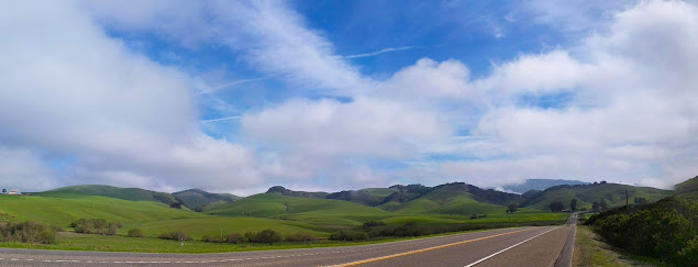 Image of a road stretching out of view and getting lost in a rolling, grassy hillside