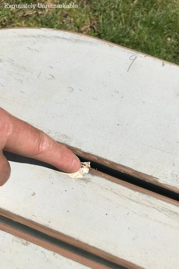 A finger applying wood putty to cracks in the wood of a bench