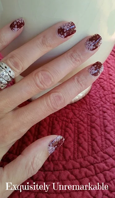 Hand wearing diamond wedding rings and floral red nail wraps