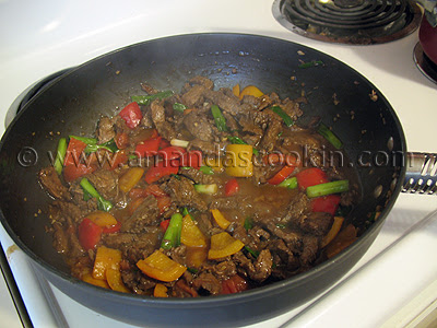 A photo of beef stir fry being cooked in a wok. 