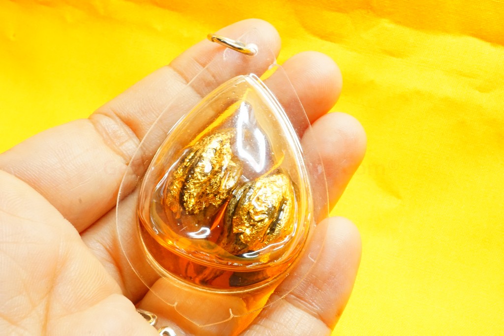  A hand holding a teardrop-shaped amulet with two golden betel nuts inside.