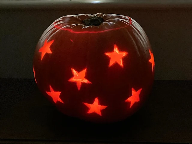 a lit up pumpkin in a dark room with star shapes all over it