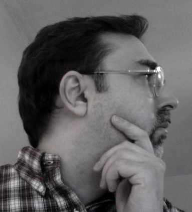 a portrait of the author in profile — male with dark hair, glasses, mustache and goatee, wearing a plaid shirt, hand resting on his chin as if in thought
