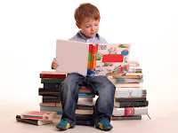young boy sitting on stack of books and reading a book