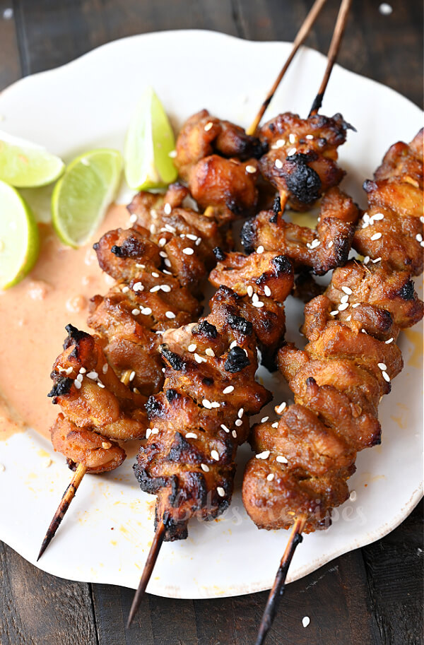 a close up of a white plate with grilled Thai coconut chicken skewers
