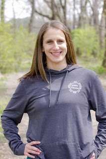 Image of a smiling white female with brown hair wearing blue long sleeved t-shirt with hands on hips