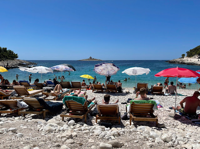 Rocky beach with umbrellas and sunbathers in Hvar, Croatia