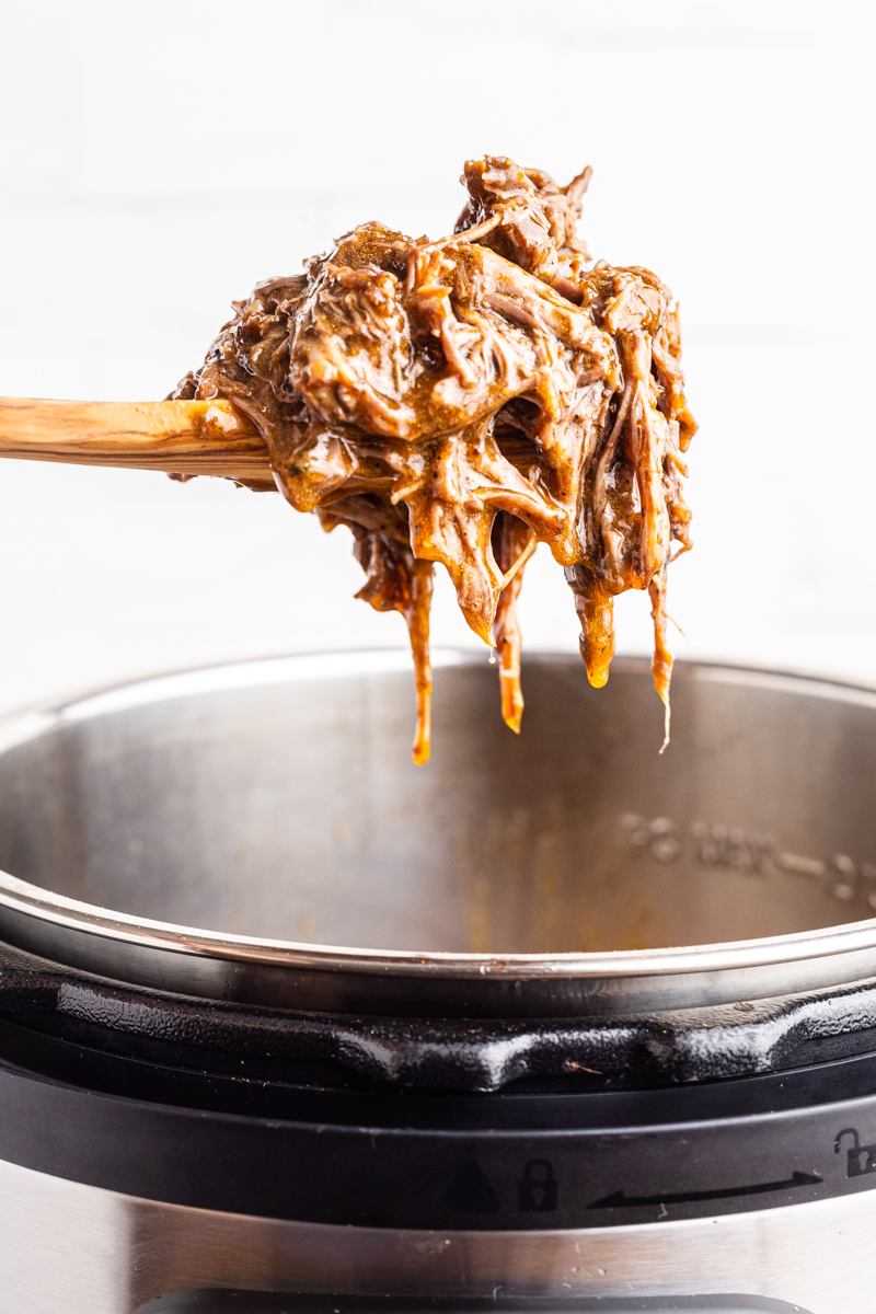 Photo of a serving spoon full of Instant Pot Mexican Shredded Beef  being help above and Instant Pot.