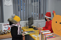 Bibliotekarka ubrana w czapkę Mikołaja wypożycza dziecku książki w Oddziale dla Dzieci Biblioteki w Zelowie.