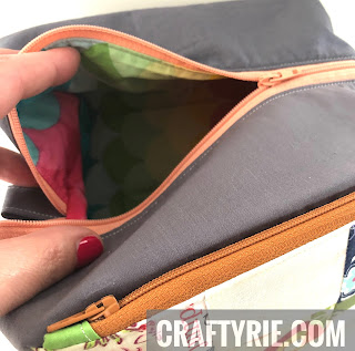 Fingers opening top zipper showing the interior of the boxy pouch
