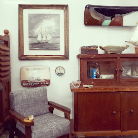 1/12 scale miniature living room with mid-century modern arm chair next to an early 20th century cabinet. Above the chair are three sailing-related pictures.