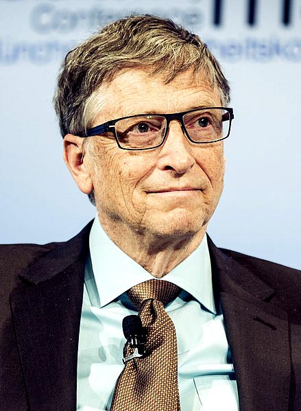 a pensive-looking older man with short, messy hair and glasses, wearing a tie with a microphone clipped to it