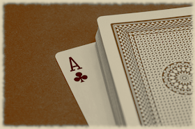 Foto: Ein Stapel Spielkarten mit der Rückseite nach oben. Die unterste Karte ist umgedreht und schaut heraus, so dass sie als Kreuz-As zu erkennen ist.